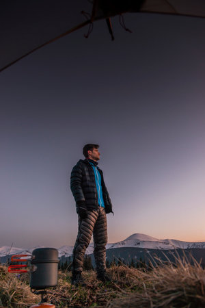 Hiker with backpack standing on top of a mountain and looking at the sunsetの写真素材