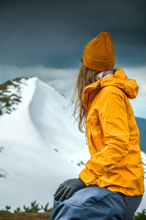 Woman hiker hiking in snowy mountain area wearing cold weather accessories, wind jacket and backpack for camping outdoor. Female portrait lifestyleの写真素材