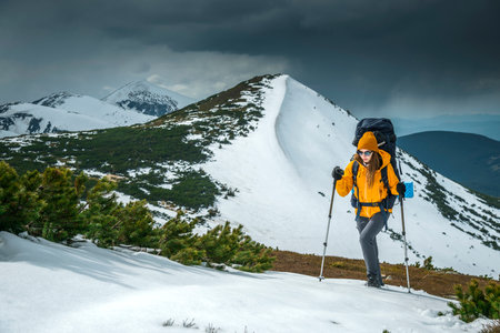 Woman hiker hiking in snowy mountain area wearing cold weather accessories, orange wind jacket. Female portrait lifestyleの写真素材