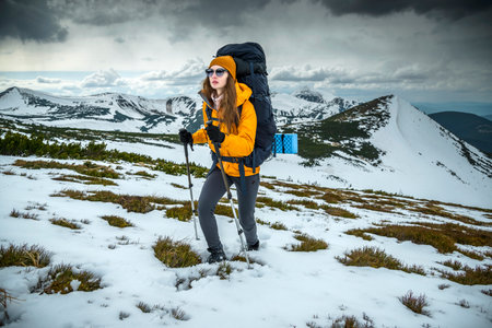 Woman hiker hiking in snowy mountain area wearing cold weather accessories, orange wind jacket. Female portrait lifestyleの写真素材