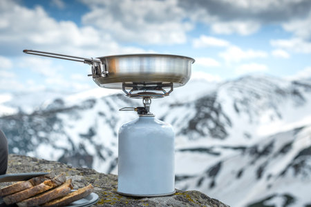 Camping fry pan on a tourist gas stove against the backdrop of snowy mountainsの写真素材