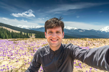 Young hiker man taking selfie while sitting on mountainside full of purple crocuses during summer hikeの写真素材