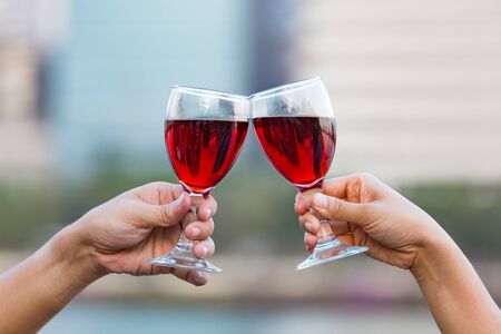 Clinking glasses of red wine in hands on nature lights backgroundの写真素材