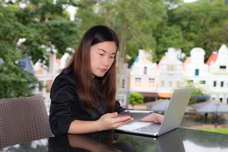 Beautiful businesswoman working on her laptop and tablet while sitting in coffee shop in a town.