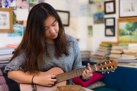 Beautiful woman relax by playing acoustic guitalele after readingÂ aÂ bookの写真素材