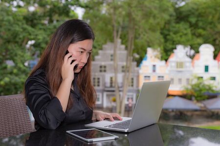 Beautiful businesswoman thinking while working on her laptop and tablet n coffee shop in a town.の写真素材