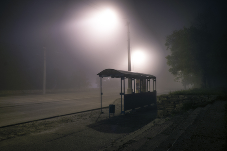 Foggy street lights misty with night deserted road and trees with bus stopの写真素材