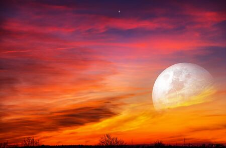 Moon in bright clouds of sunset sun. New moon. The sky at night with stars.の写真素材