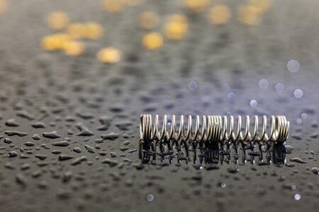 Metal spring. Precision mechanical parts. Twisted wire. Gold and silver bokeh. Part of the pen. Gold flares. Black background. Objects on a black background. Drops of water.の写真素材