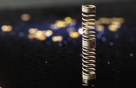 Metal spring. Precision mechanical parts. Twisted wire. Gold and silver bokeh. Part of the pen. Gold flares. Black background. Objects on a black background.の写真素材
