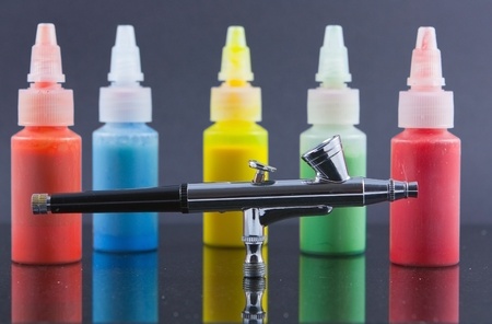 A silver airbrush against a background of out of focus and blurred bottles of spray paintの写真素材