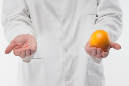 Pill in one doctors hand and orange in another, what is betterの写真素材