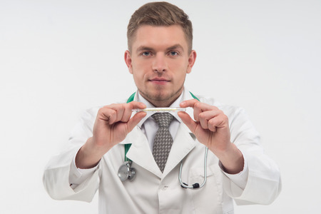 Very attractive young doctor wearing nice tie and carried the stethoscope, showing us the thermometer, necessary thing in every house  Isolated on the white の写真素材
