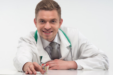 Young handsome smiling doctor, wearing beautiful tie and suggested us different colorful pills  Isolated on the white の写真素材