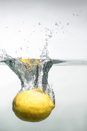 Bright yellow lemon dropped into water with splash with many bubblesの写真素材