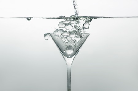 Glass of martini dipped into water with ice rising to surface of the waterの写真素材
