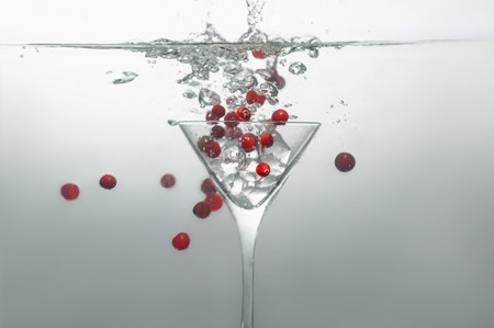 Great glass of martini with ice dipped into water with many bubbles and red berriesの写真素材