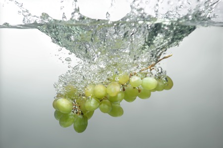 Tempting green grape dropped into the water with splash
