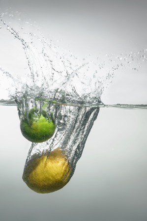 Lime and lemon falling into the water with splash and little air bubbles