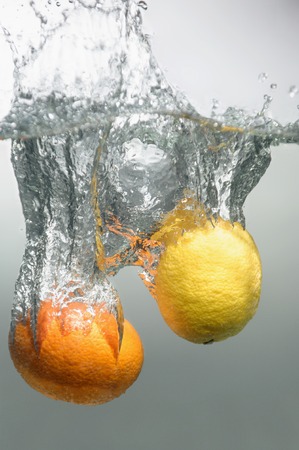Orange and lemon falling down into the water with splash and little air bubblesの写真素材