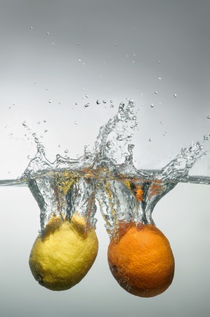 Orange and lemon falling down into the water with splash and little air bubblesの写真素材