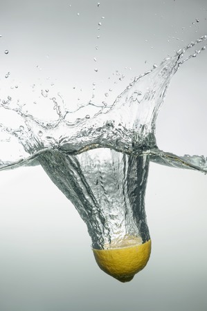 Tempting slice of lemon dropped into the water with splash and bubblesの写真素材