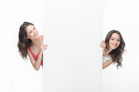 Half- length portrait of two happy curly-headed girls peering out big white poster  Isolated on the white の写真素材