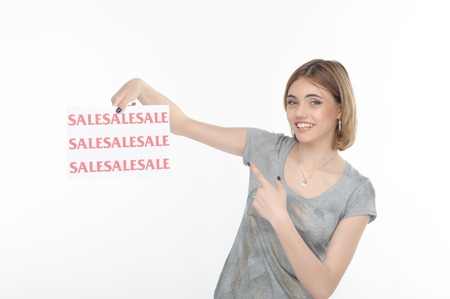 Half-length portrait of lovely smiling fair-haired girl showing us poster with SALE on it   Isolated...