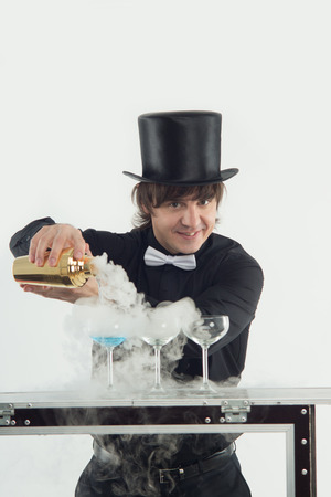 Half-length portrait of smiling dark-haired barman wearing nice black topper and shirt conjuring with his tasty blue cocktailの写真素材