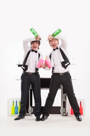 Two handsome smiling barmen standing behind the bar counter and pouring a drink into pink glasses  の写真素材