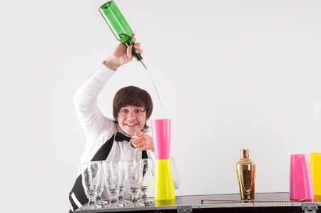 Attractive smiling barman pouring the drink into pink glass which is situated on the yellow and looking at usの写真素材