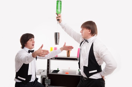 Half- length portrait of two barmen standing near the bar counter and one of them pouring a drink into the shaker in the air  の写真素材