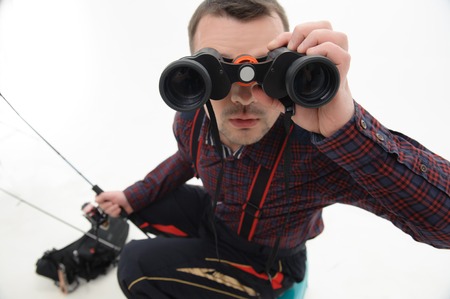Animated fisherman wearing nice checked shirt sitting on the table fishing and looking through binoculars  Isolated on white backgroundの写真素材