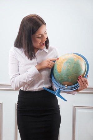 Beautiful business woman with nice haircut wearing white blouse and black skirt looking at the globe very attentively decided where she wants to travelの写真素材