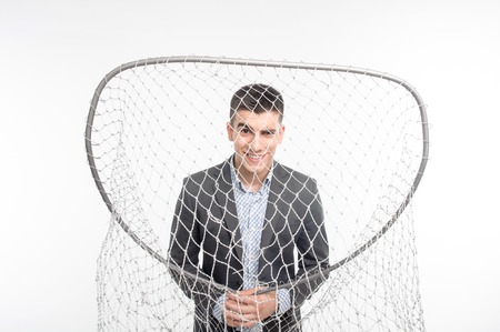 Handsome smiling man wearing good suit looking at us through big net  Concept of comparison fishing and business  Isolated on white backgroundの写真素材