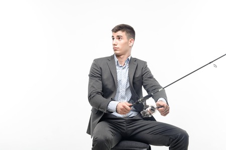 Handsome young businessman wearing stylish expensive suit holding the spinner doing his beloved work surprised someone meddling  Concept of comparison fishing and business  Isolated on white backgroundの写真素材