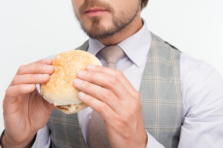 Young man wearing nice waistcoat and tie intended to eat his tasty cheeseburger  Isolated on white backgroundの写真素材