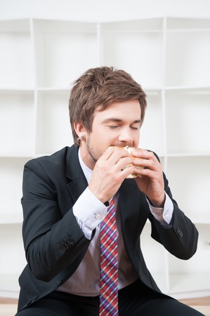 Handsome young businessman wearing great black suit and colorful tie having a snack during his lunch time in the officeの写真素材