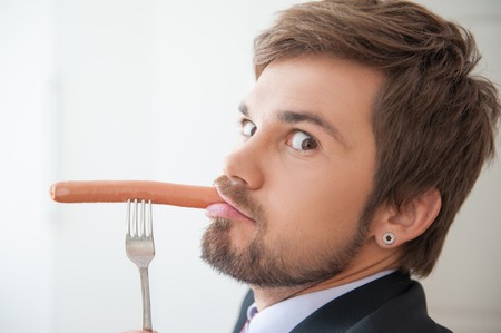 Attractive young businessman taking pleasure in very delicious sausageの写真素材