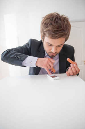 Attractive young businessman taking pleasure in very delicious sausage and in the same time dialing...