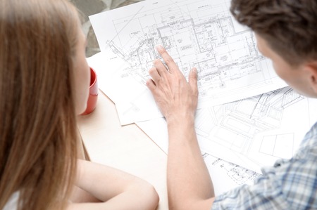 Two young architects sitting at the table with cup of coffee different plans and schemes on it discussing their new project  Top viewの写真素材