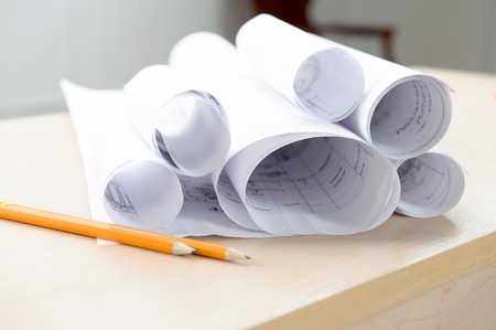 Two pens and architectonical plans and schemes rolled in a tube lying on the table
