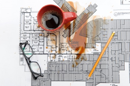 Eyeglasses pen and red cup with spilled coffee lying on the new architectonical project  Top viewの写真素材