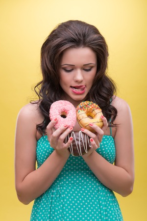 Half-length portrait of sexy dark-haired woman wearing nice mint dotted dress wanted to taste every of her doughnuts  Isolated on yellow background の写真素材