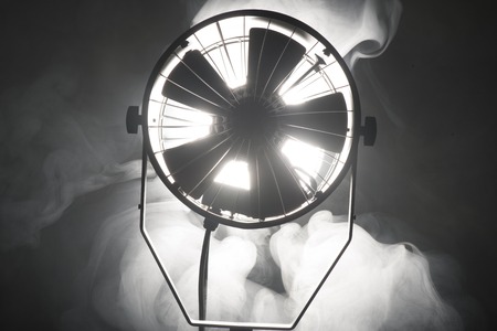Switched cinema spotlight standing in the dark enveloped in smokeの写真素材