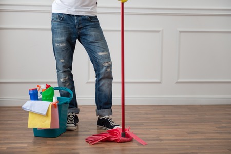 Half-length portrait of janitor wearing blue torn jeans standing with the red mop near the pail with cleansers の写真素材