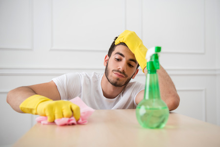 Half-length portrait of young dark-haired janitor wearing white shirt and yellow rubber gloves dusting the table very diligently の写真素材