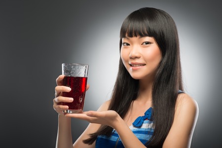 Half-length portrait of pretty young smiling dark-haired Asian woman suggested us her favorite cherry juice  Isolated on black backgroundの写真素材
