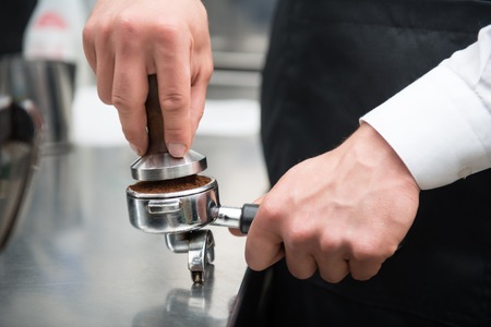 Selected focus on the hands of professional barista pressing coffee using the pounder with wooden handle  Coffee machine on backgroundの写真素材