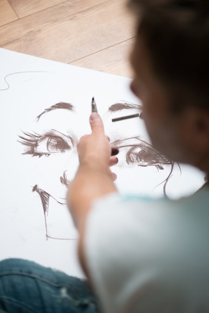 Painter drawing the picture with the lead pencil on the big white sheet of paper lying on the floor
